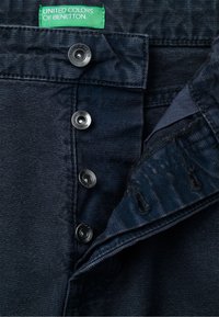 Tmavě modré džíny s knoflíkovým zapínáním se stříbrnými knoflíky a zelenou cedulkou "United Colors of Benetton" uvnitř.