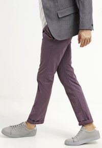 Jasnofioletowe bawełniane chinosy o dopasowanym kroju z mankietem. W zestawieniu z jasnoszarymi sneakersami niskimi, które prezentują minimalistyczny design.