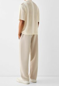Camiseta de punto color crema de manga corta con patrón de calados verticales, combinada con pantalones anchos de color beige claro y zapatillas blancas.