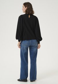 Black textured pullover with puff sleeves, featuring a keyhole back and decorative stitching. Paired with high-waisted blue wide-leg jeans.
