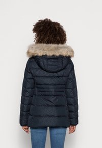 Granatowa kurtka puchowa z kapturem wykończonym futrem, pikowany o strukturze i subtelnym wzorze geometrycznym. Posiada długie rękawy oraz elastyczne mankiety.