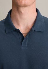 Donkerblauwe polo met een textuur gebreide stof, een twee-knopen halsopening en een klassieke kraag. Subtiele stiksel details zichtbaar bij de kraag.