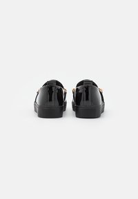 Black patent leather shoes with a flat rubber sole, featuring a gold accent on the back and a smooth, glossy finish.