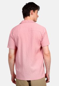 Camisa de manga corta rosa con un patrón texturizado, que presenta un cuello relajado y un dobladillo recto. Fabricada con tejido ligero.