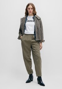 Grey suede jacket, white t-shirt with "BOSS" text, olive green trousers, and black ankle boots. Jacket features silver snaps and a floral lining.