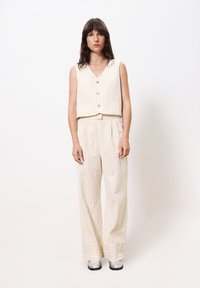 Cream-colored fabric two-piece outfit with vertical stripes; sleeveless collared vest and wide-leg trousers, complemented by shiny silver shoes.