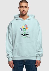 Felpa azzurra chiara con tasca frontale, caratterizzata da un design floreale e testo "Picasso" in nero. Realizzata in tessuto morbido con una vestibilità comoda.