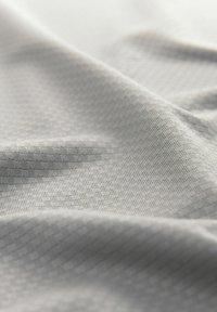 Világosszürke textile, amely finom textúrájú mintával rendelkezik, redőkbe hajtva, hogy bemutassa a mélységet és a lágy tapintást. Az anyag simának tűnik, apró részletekkel.