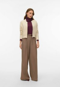 Gaiši brūns adīts kardigāns uz bordo augstās apkakles blūzes, kopā ar augsto jostasvietu, plaša kāju brūnajām biksēm. Vienkāršs dizains bez redzamām rakstainajām detaļām.