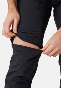 Black zip-off pants with a smooth texture, featuring a zipper at the knee. Close-up of a hand unzipping the leg section.