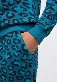 Mikina a nohavice s tyrkysovým leopardím vzorom, s rebrovanými manžetami a bočným vreckom. Materiál je mäkký a hladký na dotyk.