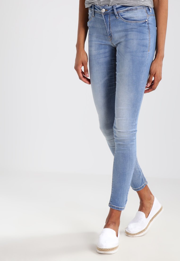Vaqueros de mezclilla azul claro con corte slim, diseño de cinco bolsillos, sutil desvanecimiento y cintura de altura media, combinados con zapatos de esparto blancos.