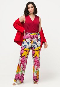 Top rosso senza maniche abbinato a pantaloni larghi con un motivo floreale nei colori rosa, giallo, blu e verde. Include una cintura coordinata e sandali bianchi.