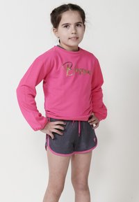 Sweatshirt rose à manches longues avec "Blossom" en écriture dorée, associé à un short gris avec des bordures roses et un cordon de serrage. Texture lisse.