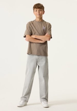 Bruin T-shirt met korte mouwen en een logo op de borst; lichtgrijze spijkerbroek; witte sneakers; casual pasvorm en een ontspannen silhouet.
