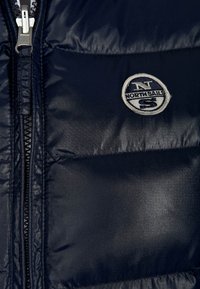 Námořnická modrá péřová bunda s horizontálním prošíváním, se zipem vpředu a kulatým logem North Sails na levé části hrudi.