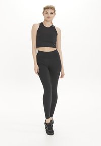 Svart kort tanktop och högmidjade leggings, båda gjorda av stretchigt tyg. Outfiten har en sömlös design och en figurnära siluett.