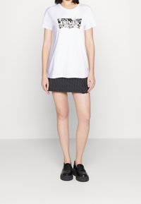 Bílá bavlněná tričko s barevným logem Levi’s, spárované s černou sukní s jemným proužkem a černými mokasíny.