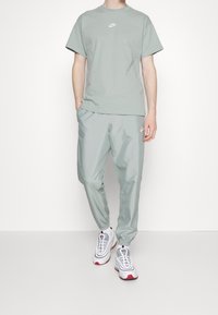 Ljusgrön bomulls-T-shirt med vitt Nike-logotyp, matchad med ljusgröna joggers. Nike-sneakers med vita, grå och röda detaljer.