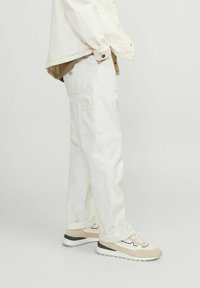 White cargo pants with side pockets, paired with beige and white sneakers. The jacket is off-white denim with a brown shirt underneath.