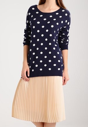 Marineblauwe trui met witte stippen, ronde hals en geribde manchetten, gecombineerd met een beige geplooide midi-jurk. Soepele stoftextuur.