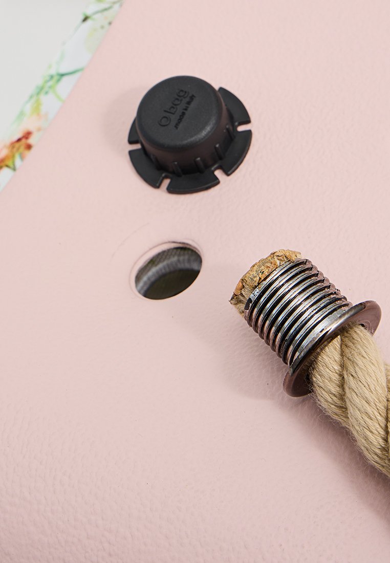 Różowa powierzchnia z czarnym okrągłym zaworem i metalowym złączem z skręconym sznurkiem. Zbliżenie ukazuje tekstury i funkcjonalne elementy.