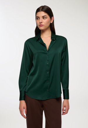Blusa di raso verde scuro con colletto, maniche lunghe e chiusura a bottoni. Il tessuto ha una consistenza liscia e una leggera lucentezza.