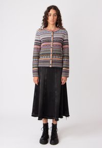 Cardigan lavorato a maglia con motivi multicolore, base grigia, con chiusura a bottone. Abbinato a una gonna di jeans nera e stivali neri con lacci.