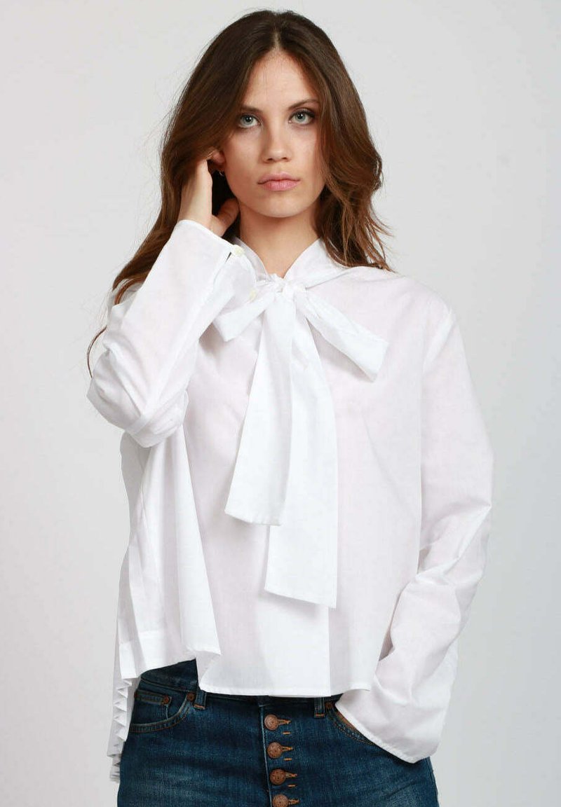 Blusa bianca con fiocco al collo, maniche lunghe e dettagli con bottoni. Abbinata a jeans denim blu con cinque bottoni sul davanti.