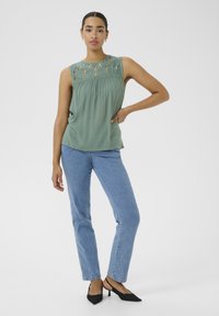 Grön ärmlös blus med spetsdetaljer vid kragen, tillsammans med ljusblå denimjeans och svarta spetsiga mules.
