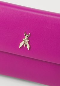 Portefeuille en cuir fuchsia avec une finition texturée, présentant un charme insecte métallique comme accent décoratif sur le devant.