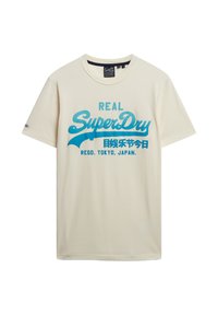 Camiseta de algodón crema con un estampado gráfico azul que dice "REAL SuperDry" con texto adicional. Diseño de manga corta y cuello redondo.