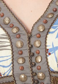 Tela gris con costura decorativa, adornada con botones marrones y metálicos, un diseño de escote en V y acentos florales en azul y rojo.