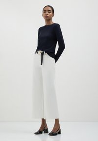 Maglione a maniche lunghe blu navy, pantaloni larghi bianchi con una cintura nera e scarpe con tacco nere. Design semplice e colori a contrasto.