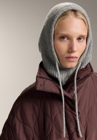 Steppelt barna pufidzseki magas gallérral, szürke kötött kapucnival, húzózsinórral és texturált anyaggal. Egyszerű, modern dizájn.