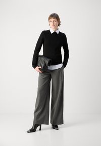 Svart strikket genser med hvit krage, grå vide bukser og svarte hæler med metalliske detaljer; holder en svart clutch-veske.