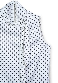Blusa senza maniche bianca con pois neri, caratterizzata da un fiocco al collo e una texture di tessuto liscia e lucida.