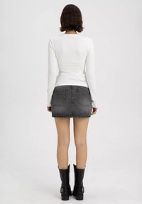 Weißes Langarmoberteil kombiniert mit einem grauen Jeans-Minirock, der über Rückentaschen verfügt, und schwarzen Stiefeletten mit robusten Sohlen.