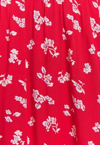 Tessuto rosso con un motivo floreale in bianco e azzurro chiaro. La trama sembra tessuta e presenta piccoli fiori e foglie sparsi.