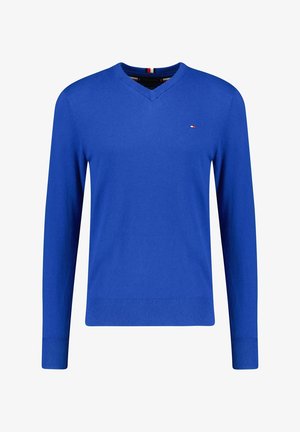 Modrý svetr s dlouhým rukávem a V výstřihem, s malým červeným, bílým a modrým logem na levé straně hrudi a žebrovanými manžetami a lemem.