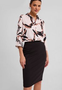 Wielokolorowa bluzka z abstrakcyjnymi wzorami w czerni, brązie i różu, sparowana z dopasowaną czarną spódnicą ołówkową. Obie odzież mają gładkie faktury.