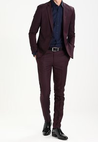 Burgundyfärgad kostym med slim fit, tillsammans med en mörkblå skjorta. Svarta läderskor och ett svart bälte fulländar looken.