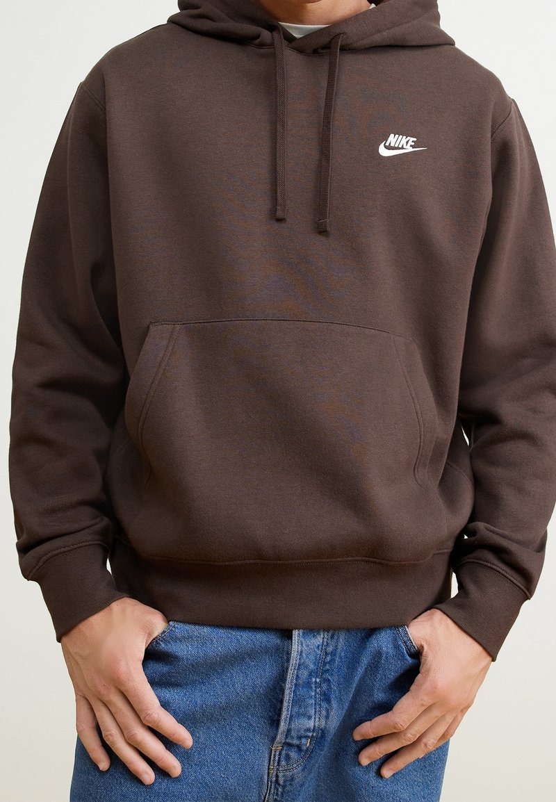 Brauner Hoodie mit einer vorderen Tasche, Kordelzugkapuze und einem weißen Nike-Logo auf der Brust. Hergestellt aus weichem Stoff, mit gerippten Bündchen und Saum.