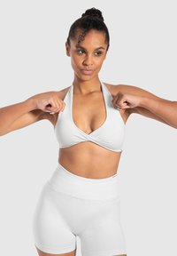 Vit halterneck sportbh med en invecklad design, i kombination med högmidjade vita shorts. Slät textur, minimalistisk stil, inga synliga mönster.