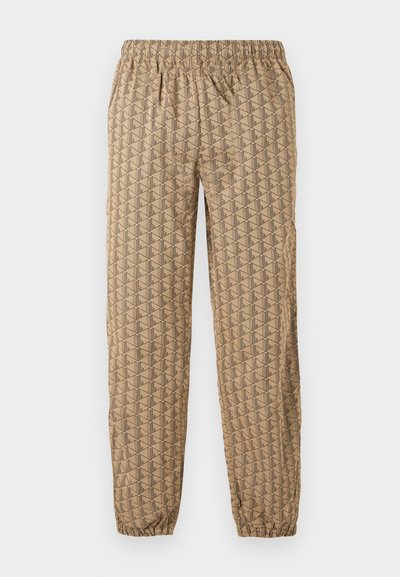 Pantalon de jogging beige avec taille élastique et chevilles élastiques, présentant un motif géométrique répétitif de formes stylisées en "B" marron foncé.