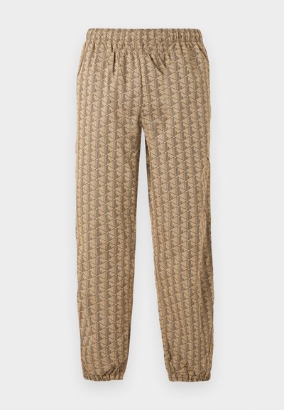 Pantalon de jogging beige avec taille élastique et chevilles élastiques, présentant un motif géométrique répétitif de formes stylisées en "B" marron foncé.