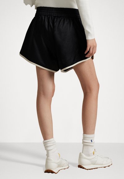 Zwarte sportshorts met een gestructureerde afwerking en witte details, met een elastische tailleband. Gevergd met witte sneakers en sokken.