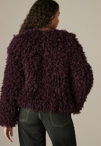 Lilla, fluffy strikket sweater med lange ærmer og rund halsudskæring, vist fra ryggen, parret med mørke denimbukser.