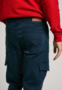 Pantalones cargo azul marino con una textura suave, que cuentan con bolsillos laterales y un parche de cuero marrón con el logo en la parte trasera de la cinturilla.