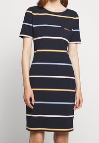 Niebieska sukienka w paski z bawełny z poziomymi paskami w kolorze pomarańczowym, jasnoróżowym i niebieskim. Okrągły dekolt i krótkie rękawy z kieszonką na piersi.